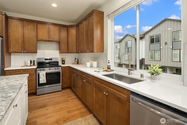 kitchen featuring light wood-style flooring, a sink, light countertops, appliances with stainless steel finishes, and backsplash