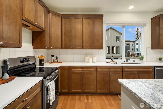 kitchen with light wood-style flooring, a sink, decorative backsplash, light countertops, and appliances with stainless steel finishes