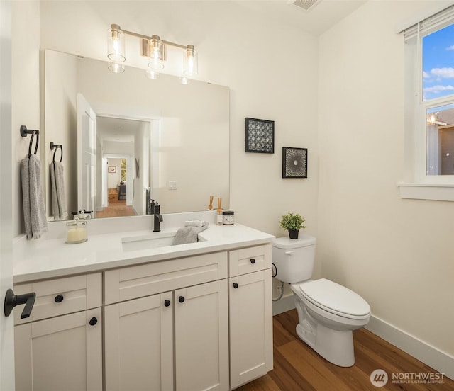 bathroom featuring visible vents, baseboards, toilet, wood finished floors, and vanity