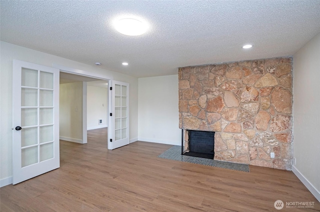 unfurnished living room with a textured ceiling, wood finished floors, french doors, a stone fireplace, and baseboards