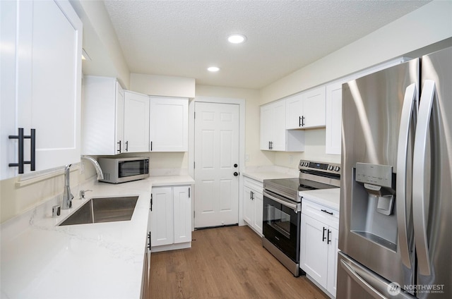 kitchen with white cabinets, wood finished floors, appliances with stainless steel finishes, and a sink