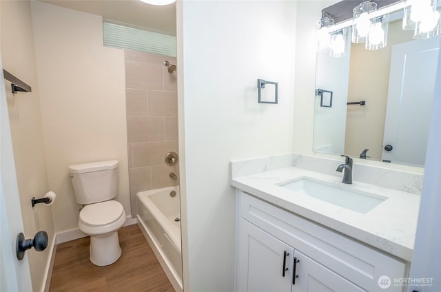 bathroom with toilet, wood finished floors,  shower combination, baseboards, and vanity