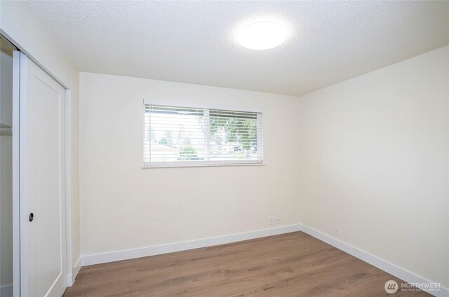 unfurnished bedroom with a closet, baseboards, a textured ceiling, and wood finished floors