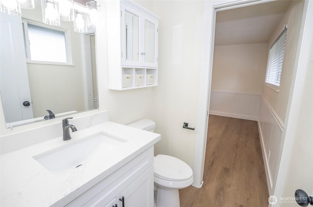 bathroom with a wainscoted wall, plenty of natural light, toilet, and wood finished floors