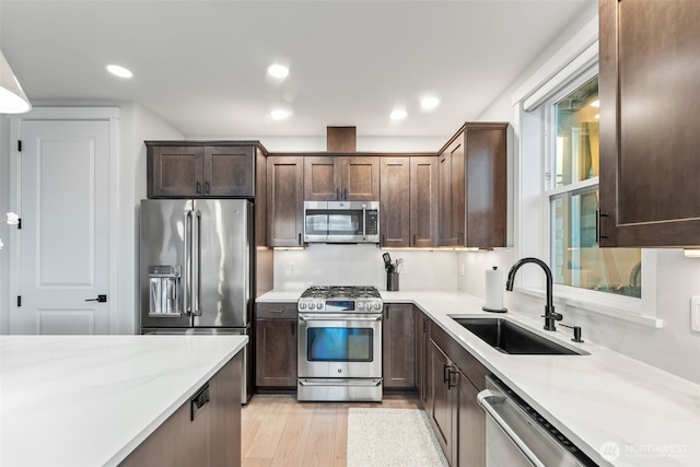 kitchen with light wood-type flooring, a sink, appliances with stainless steel finishes, light stone countertops, and dark brown cabinets