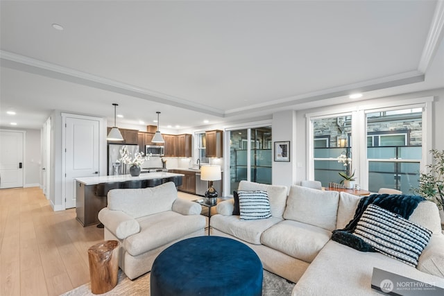 living room featuring light wood finished floors, crown molding, baseboards, recessed lighting, and a raised ceiling