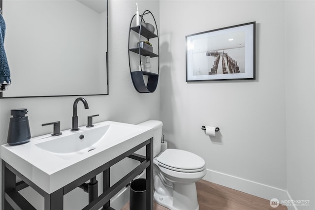 bathroom with a sink, toilet, baseboards, and wood finished floors