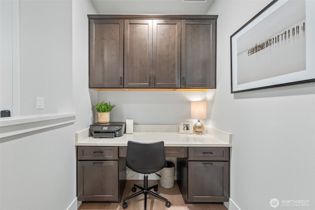 office with visible vents, baseboards, wood finished floors, and built in study area