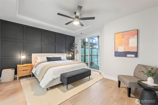 bedroom featuring baseboards, access to exterior, a raised ceiling, a decorative wall, and light wood-type flooring