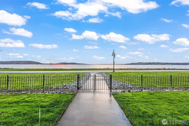 view of home's community with a gate, fence, a water view, and a lawn