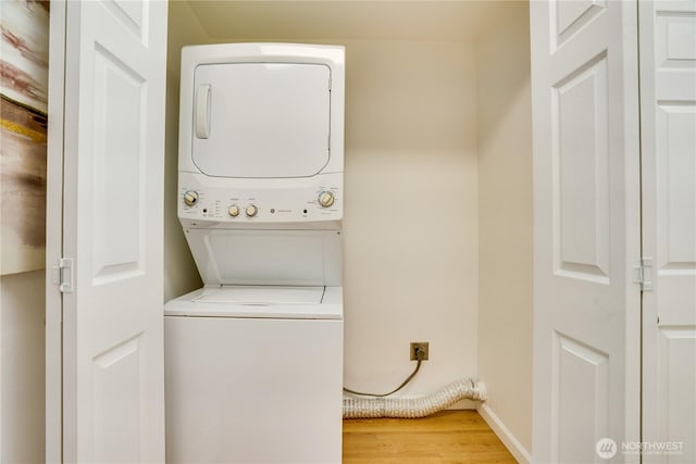 clothes washing area with laundry area, light wood-style flooring, baseboards, and stacked washer and clothes dryer