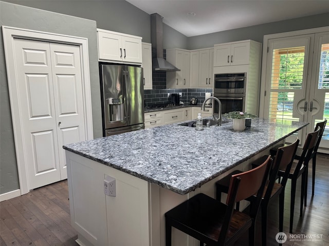 kitchen featuring a sink, backsplash, stainless steel appliances, white cabinets, and wall chimney range hood