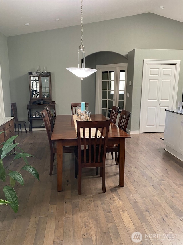 dining room with baseboards, light wood-style floors, and vaulted ceiling