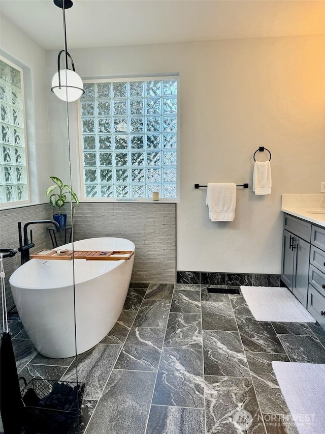 full bathroom with marble finish floor, vanity, and a freestanding tub