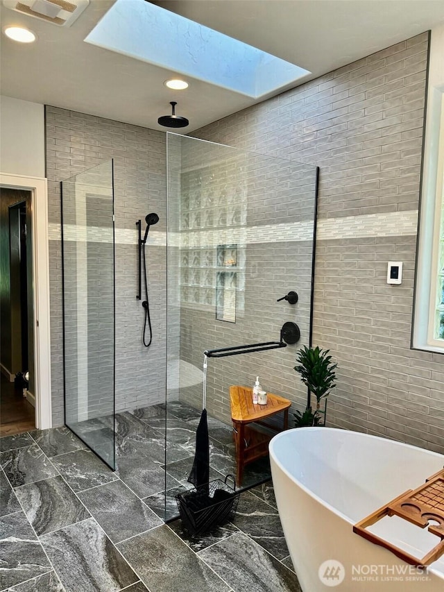 bathroom with visible vents, a freestanding tub, a walk in shower, tile walls, and marble finish floor