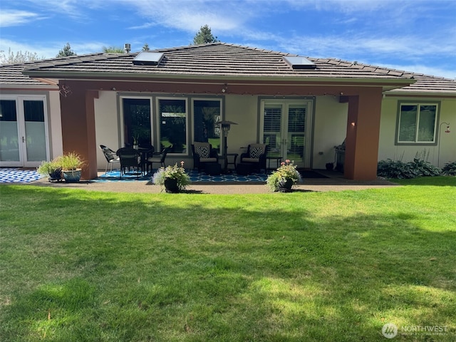 rear view of property with a tiled roof, a yard, french doors, and a patio