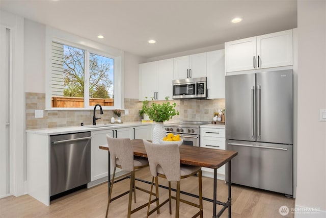 kitchen with premium appliances, light wood-type flooring, light countertops, and a sink