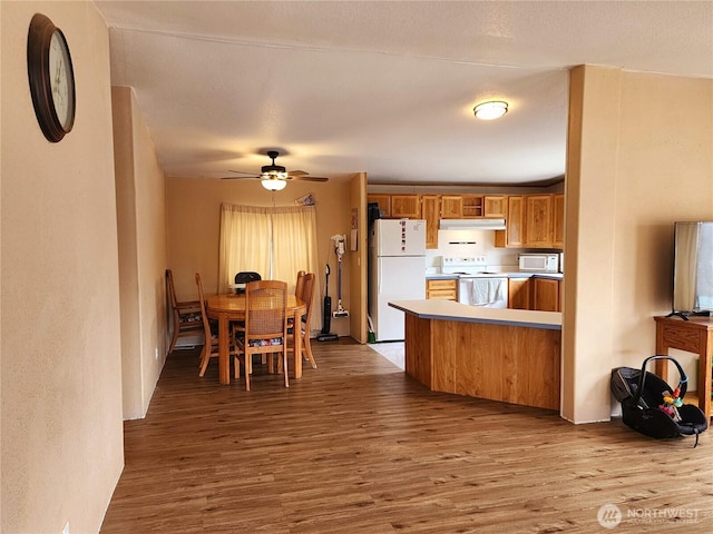 kitchen featuring white appliances, brown cabinetry, wood finished floors, ceiling fan, and under cabinet range hood