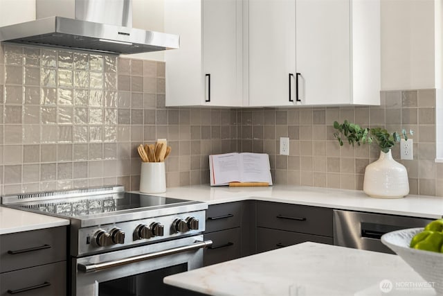 kitchen featuring light countertops, decorative backsplash, range hood, gray cabinets, and stainless steel appliances