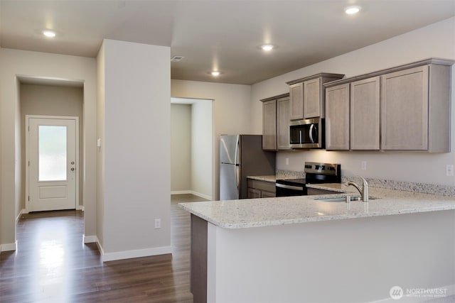 kitchen with a sink, light stone counters, a peninsula, stainless steel appliances, and dark wood-style flooring