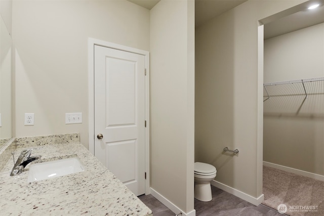 bathroom featuring a walk in closet, baseboards, toilet, and vanity