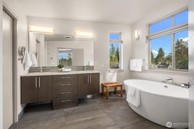 full bath with visible vents, a sink, backsplash, double vanity, and a freestanding bath