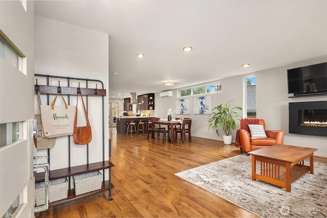 living area featuring a glass covered fireplace, an AC wall unit, wood finished floors, and recessed lighting