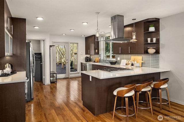 kitchen with a sink, island range hood, light countertops, decorative backsplash, and dark brown cabinets