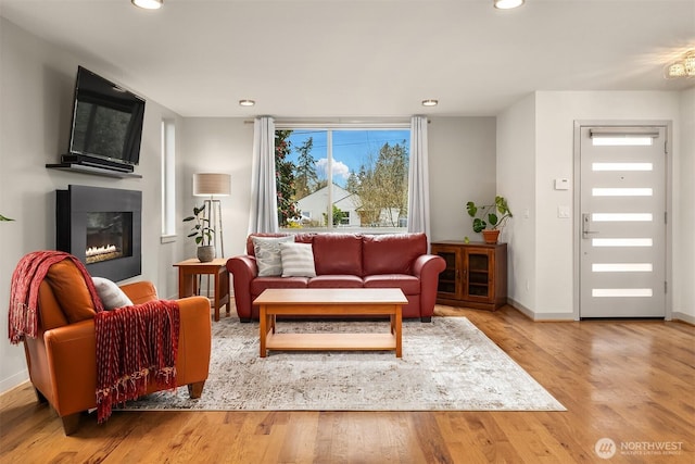 living area with a glass covered fireplace, recessed lighting, and wood finished floors