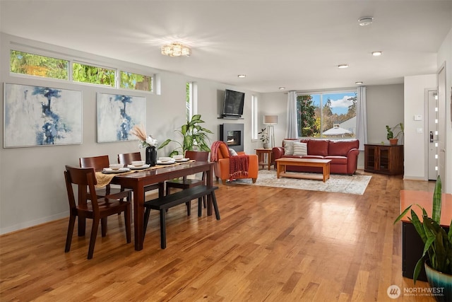 dining area with a glass covered fireplace, baseboards, light wood-style flooring, and recessed lighting