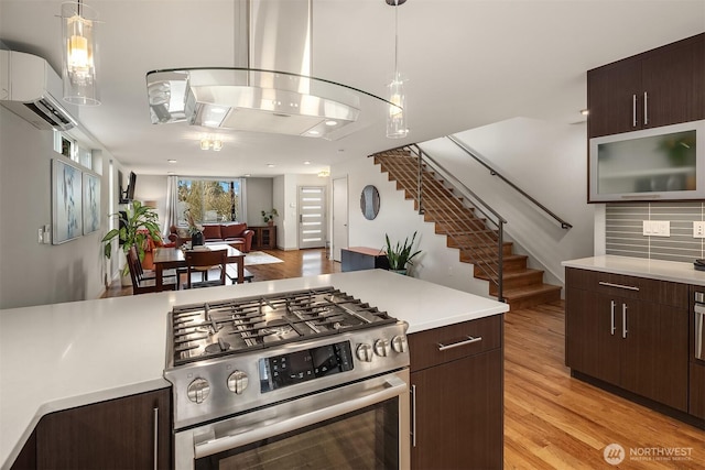 kitchen with dark brown cabinets, stainless steel gas range, a wall mounted AC, and light countertops