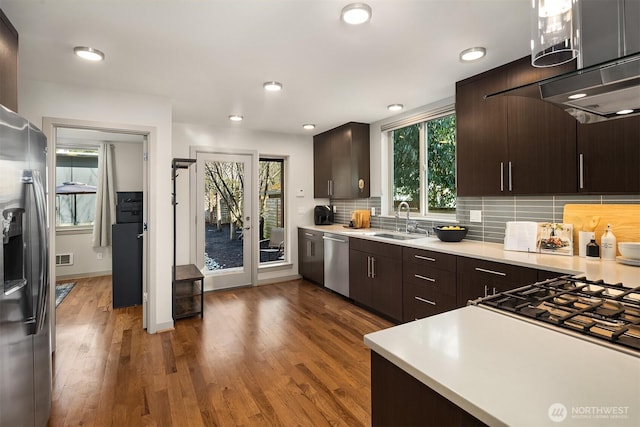 kitchen with a sink, backsplash, dark brown cabinetry, appliances with stainless steel finishes, and light countertops