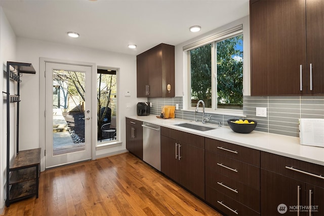 kitchen featuring light countertops, decorative backsplash, stainless steel dishwasher, wood finished floors, and a sink