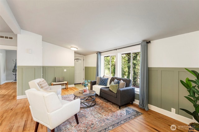 living room with visible vents, lofted ceiling, light wood-style floors, and a wainscoted wall