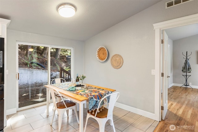 dining area featuring visible vents, light wood-style flooring, lofted ceiling, and baseboards