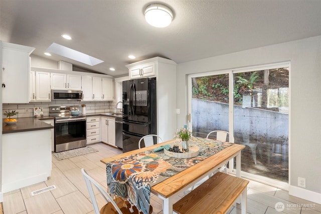 kitchen featuring visible vents, vaulted ceiling with skylight, stainless steel appliances, dark countertops, and tasteful backsplash