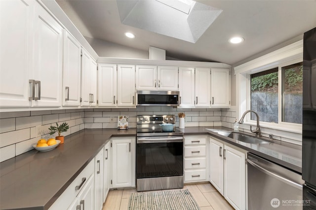 kitchen featuring dark countertops, vaulted ceiling with skylight, appliances with stainless steel finishes, and a sink