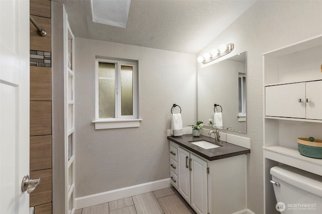 bathroom with vanity, baseboards, a textured ceiling, toilet, and a textured wall