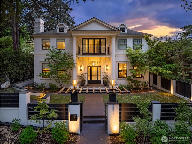 neoclassical / greek revival house featuring a fenced front yard, stucco siding, a chimney, and a balcony