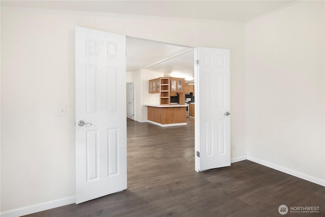 empty room with dark wood-style floors, baseboards, and ornamental molding