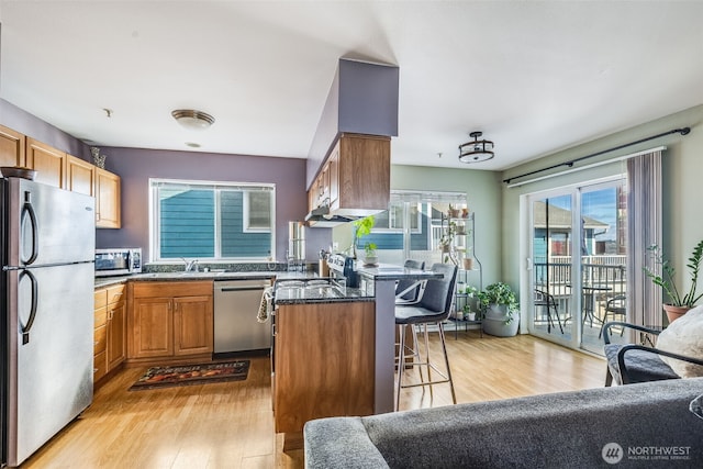 kitchen featuring a kitchen bar, brown cabinets, appliances with stainless steel finishes, and light wood-style flooring