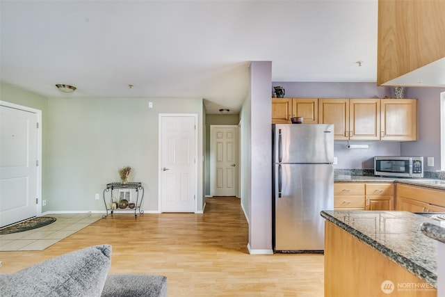 kitchen with light wood-type flooring, light brown cabinetry, stone countertops, stainless steel appliances, and baseboards