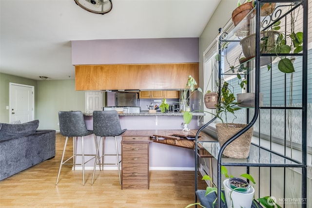 kitchen featuring light stone counters, brown cabinetry, a breakfast bar, a peninsula, and light wood-style flooring