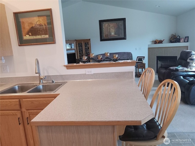 kitchen featuring a sink, open floor plan, a peninsula, a fireplace, and vaulted ceiling