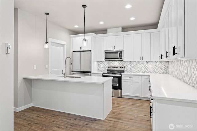 kitchen featuring a sink, white cabinetry, stainless steel appliances, light wood-style floors, and a peninsula