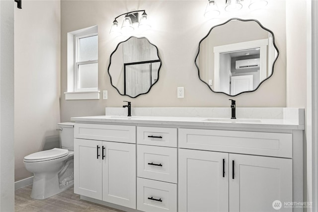 bathroom with toilet, a wall unit AC, double vanity, wood finished floors, and a sink