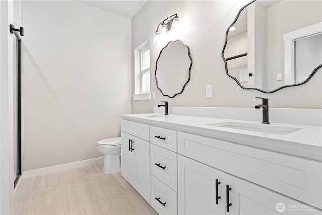 bathroom featuring double vanity, toilet, baseboards, and a sink