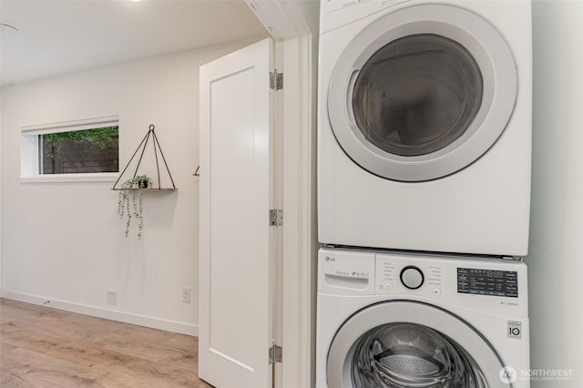 laundry room featuring light wood-type flooring, baseboards, stacked washer and clothes dryer, and laundry area