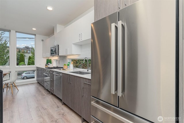 kitchen featuring tasteful backsplash, light countertops, light wood-style flooring, stainless steel appliances, and a sink