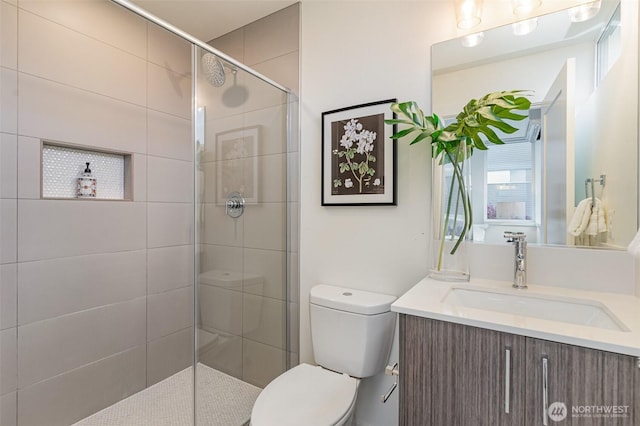 bathroom featuring toilet, vanity, and a tile shower